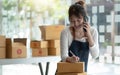 Happy young Asian business owner woman prepare parcel box and check online orders of product for deliver to customer on smartphone Royalty Free Stock Photo