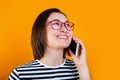 Happy young asian business woman in red glasses talking by mobile phone on yellow background. Royalty Free Stock Photo