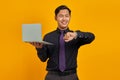 Happy young Asian businessman looking at wristwatch and holding laptop isolated on yellow background Royalty Free Stock Photo