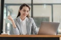 Happy young asian businesswoman celebrating success with arms raised in front of laptop with excitement at office Royalty Free Stock Photo