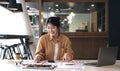 Happy young asian businesswoman sitting on her workplace and using calculator in the office. Young woman working at laptop in the Royalty Free Stock Photo