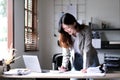 Happy young Asian businesswoman standing using calculator and laptop computer at office. Royalty Free Stock Photo