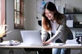 Happy young Asian businesswoman standing using calculator and laptop computer at office. Royalty Free Stock Photo