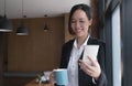 Happy young Asian businesswoman standing using smartphone and hold coffee cup at office. Royalty Free Stock Photo