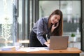 Happy young Asian businesswoman standing using smartphone and laptop computer at office. Royalty Free Stock Photo