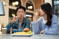 Happy young Asian couple enjoying eating fries, dating, and having lunch at a restaurant together Royalty Free Stock Photo