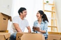Happy young Asian couple moving in to new house, using digital tablet organizing things and unpacking boxes together