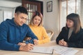 Happy young Asian couple and realtor agent. Cheerful young man signing some documents while sitting at desk together with his wife Royalty Free Stock Photo