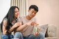 A happy young Asian couple is saving some money in a jar while talking about their savings plan Royalty Free Stock Photo