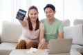 Happy young asian couple sitting on sofa show calculator with income and profit in living room at home. Royalty Free Stock Photo