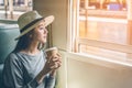 Happy young Asian cute woman sitting, holding coffee cup and looking outside the window train. Travel summer and holiday concept Royalty Free Stock Photo