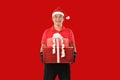 Happy young Asian delivery man in red uniform, Christmas hat carry boxes of presents in hands on red background during Christmas f