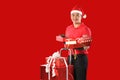 Happy young Asian delivery man in red uniform, Christmas hat carry boxes of presents in hands on red background during Christmas f