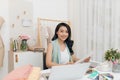 Happy young Asian designer in casualwear sitting by desk and making fashion sketches Royalty Free Stock Photo