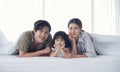 Happy young Asian family father mother and daughter are lying under white blanket on bed in the bedroom Royalty Free Stock Photo