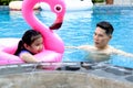 Happy young Asian father and little girl daughter with pink flamingo plastic toy in blue water pool, dad teaching child kid Royalty Free Stock Photo