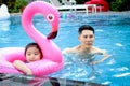 Happy young Asian father and little girl daughter with pink flamingo plastic toy in blue water pool, dad teaching child kid Royalty Free Stock Photo