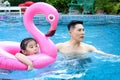 Happy young Asian father and little girl daughter with pink flamingo plastic toy in blue water pool, dad teaching child kid Royalty Free Stock Photo