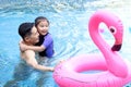 Happy young Asian father and little girl daughter with pink flamingo plastic toy in blue water pool, dad teaching child kid Royalty Free Stock Photo