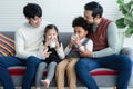 Happy young Asian gay couple with diverse adopted children, African and Caucasian, drinking milk and sitting on sofa at home. Royalty Free Stock Photo