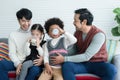 Happy young Asian gay couple with diverse adopted children, African and Caucasian, drinking milk and sitting on sofa at home. Royalty Free Stock Photo