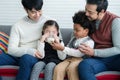 Happy young Asian gay couple with diverse adopted children, African and Caucasian, drinking milk and sitting on sofa at home. Royalty Free Stock Photo