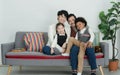 Happy young Asian gay couple with diverse adopted children African and Caucasian smiling sitting on sofa at home Royalty Free Stock Photo