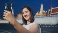 Happy young Asian girl tourist with casual style hold mobile phone take selfie photo peaceful picture of background temple in