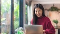 Happy young Asian girl working at a coffee shop with a laptop .Woman happy smiling to camera in cafe day.