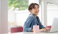 Happy young Asian girl working at a coffee shop with a laptop .Woman happy smiling to camera in cafe day. Royalty Free Stock Photo