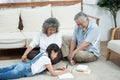 Happy young asian granddaughter reading and writing book with grandfather and grandmother looking beside on floor in living room Royalty Free Stock Photo