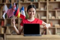 Happy young asian lady student with many international flags show finger at laptop with empty screen