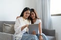 Happy young asian lesbian couple hugging having fun using digital tablet relaxing on couch at home. Two smiling women Royalty Free Stock Photo