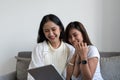 Happy young asian lesbian couple hugging having fun using digital tablet relaxing on couch at home. Two smiling women Royalty Free Stock Photo