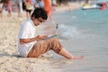 Happy young Asian man with computer laptop on the sandy beach in summer time. Summer vacations and lifestyle concept