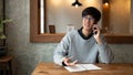 A happy young Asian man is talking on the phone with someone while working remotely at a coffee shop Royalty Free Stock Photo