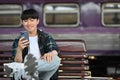 Happy young Asian man traveling by himself with backpack, using mobile phone at train station Royalty Free Stock Photo