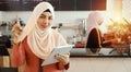 Happy young asian muslim advanced employee barista user of technology holding tablet, wearing white hijab and pointing something