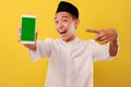 Happy Young Asian Muslim man showing blank green phone screen and pointing phone screen Royalty Free Stock Photo