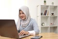 Happy young Asian muslim woman freelancer working on computer at home. Attractive businesswoman studying online, using laptop Royalty Free Stock Photo