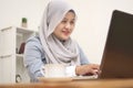 Happy young Asian muslim woman freelancer working on computer at home. Attractive businesswoman studying online, using laptop Royalty Free Stock Photo