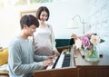 Happy young asian pregnant woman stand side of man play piano at home. Pregnancy, motherhood, people, love, expectation, family - Royalty Free Stock Photo