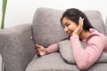 Happy young asian teen girl sit on sofa at home holding phone looking at screen waving hand video calling distance Royalty Free Stock Photo