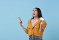 Happy young Asian teen woman laughing holding mobile phone and credit card isolated on studio blue background Royalty Free Stock Photo