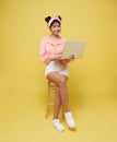 Happy young Asian teen woman smiling. While her using laptop sitting on white chair isolate on bright yellow background Royalty Free Stock Photo