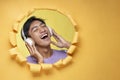 Happy young Asian teenager man singing a song poses through torn yellow paper hole with a copy space, wearing purple t-shirt and Royalty Free Stock Photo