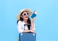 Happy young Asian tourist woman holding passport and boarding pass with baggage going to travel on holidays on blue background Royalty Free Stock Photo