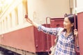 Happy young Asian traveller woman taking selfie photo from mobile phone at train station while traveling