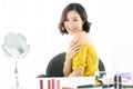 Happy young Asian woman applying cream to arm on with mirror for makeup routine and looking at camera at home. Beauty, skin care Royalty Free Stock Photo