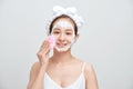 Happy young Asian woman applying foaming cleanser on her face and wearing towel on her head